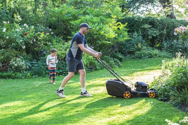 Photo of man mowing lawn while son watches