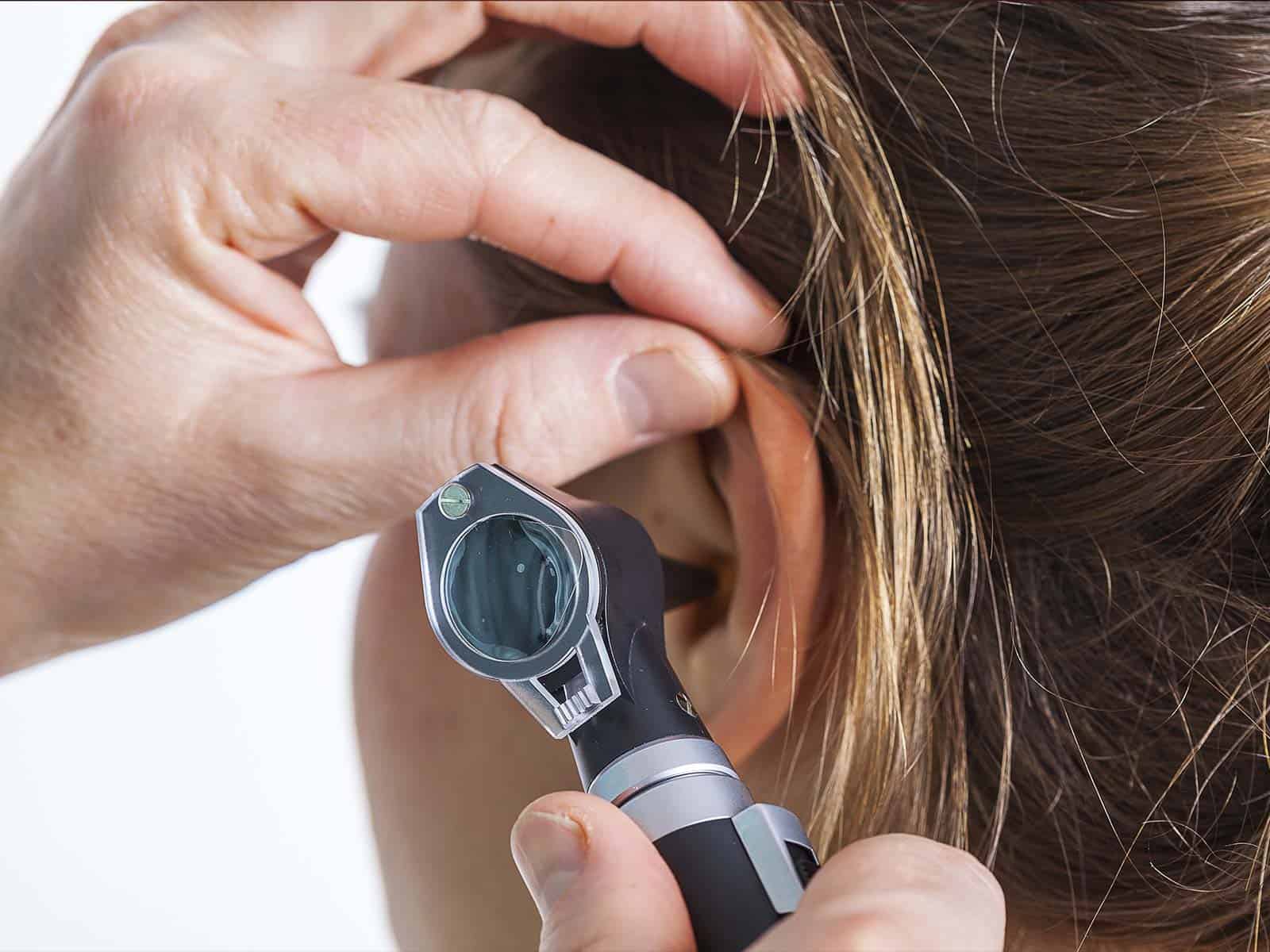 A photo of a lady having her ear checked by a doctor