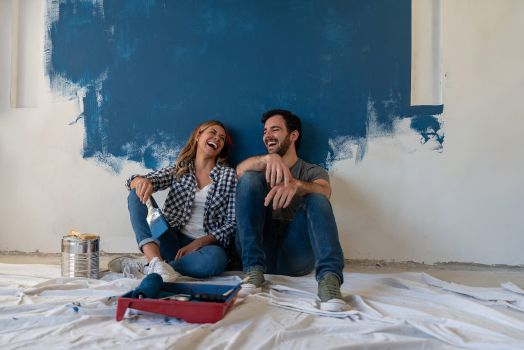 Portrait of a happy couple laughing while taking a break from painting - home improvement concepts