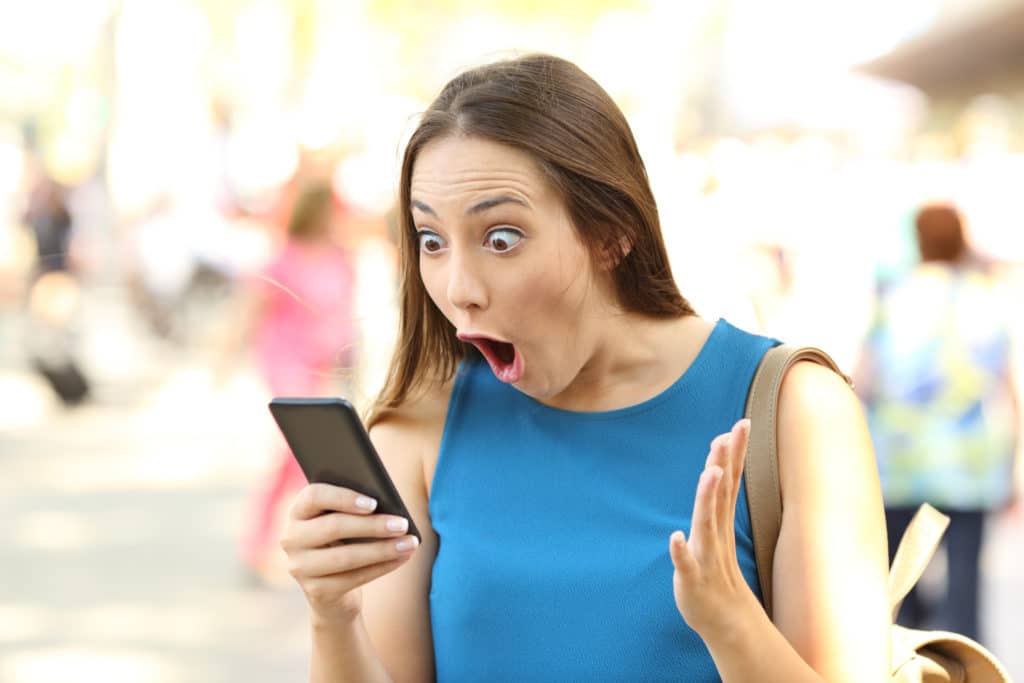 Amazed woman receiving shocking news on a smart phone on the street